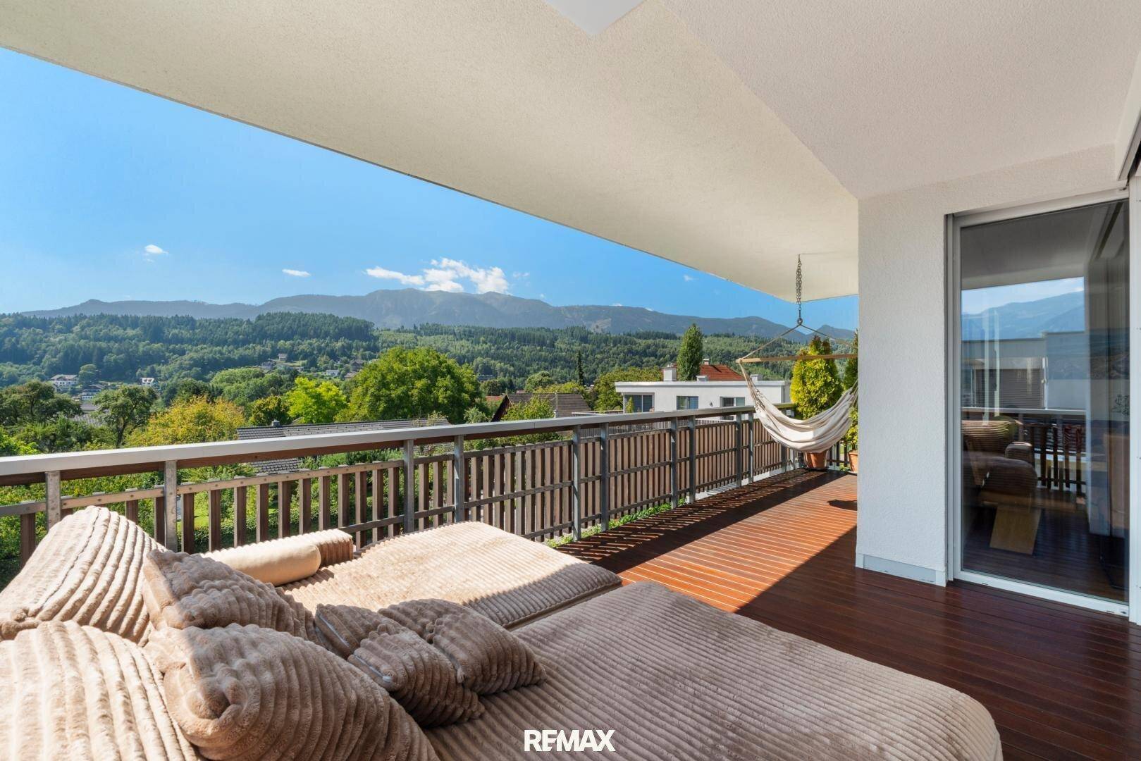 Geräumiger Balkon mit Holzboden, Liegemöbeln und weitem Blick auf die bewaldeten Berge.