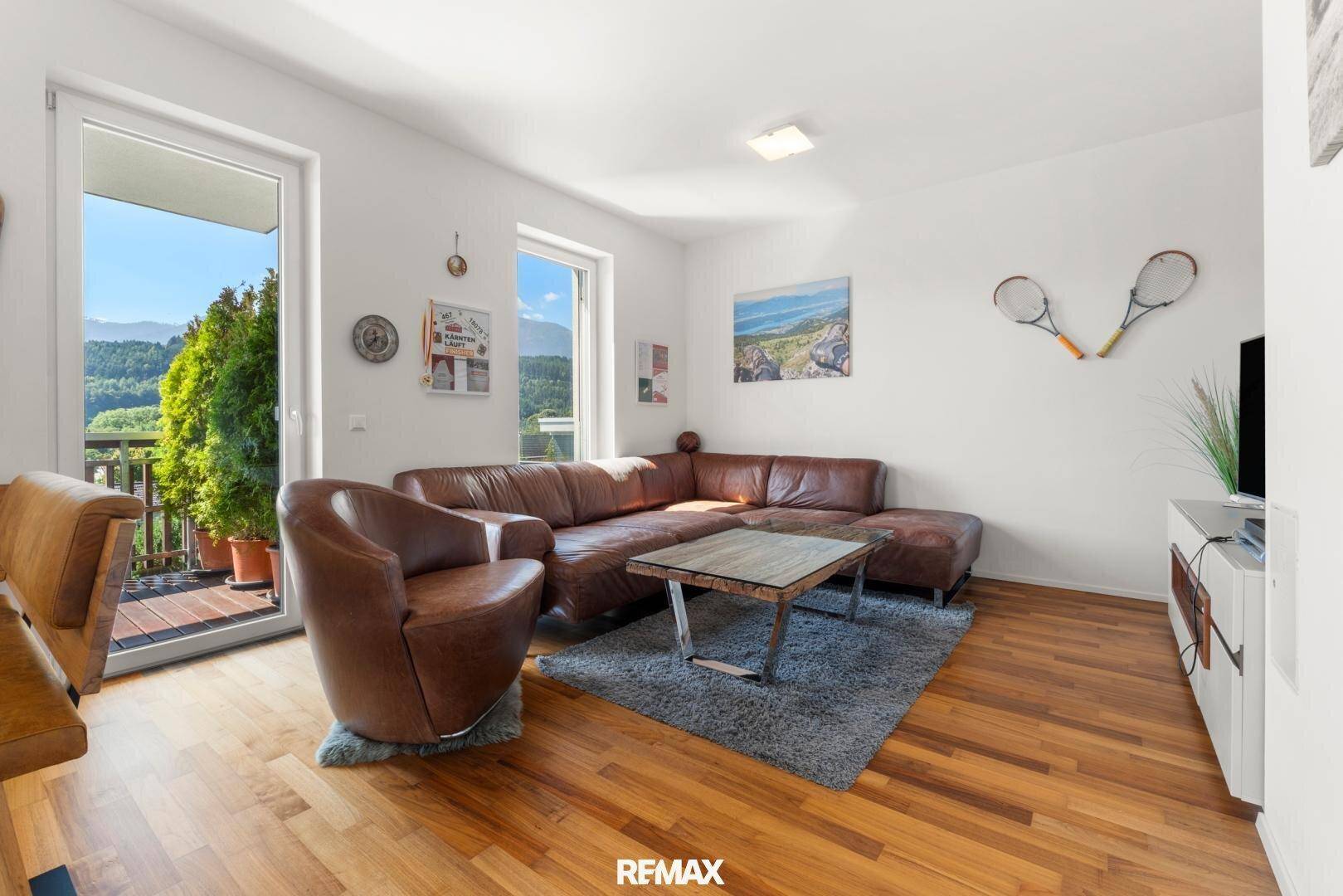 Geräumiges Wohnzimmer mit Ledersofa, Holzboden und Zugang zu einem Balkon mit Bergblick.