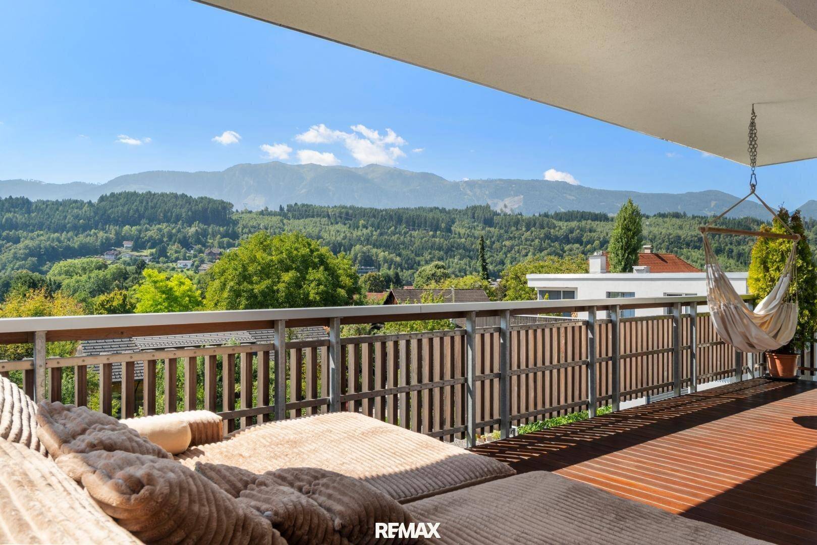 Geräumiger Balkon mit Holzboden, Hängematte und weitem Blick auf die bewaldeten Berge.