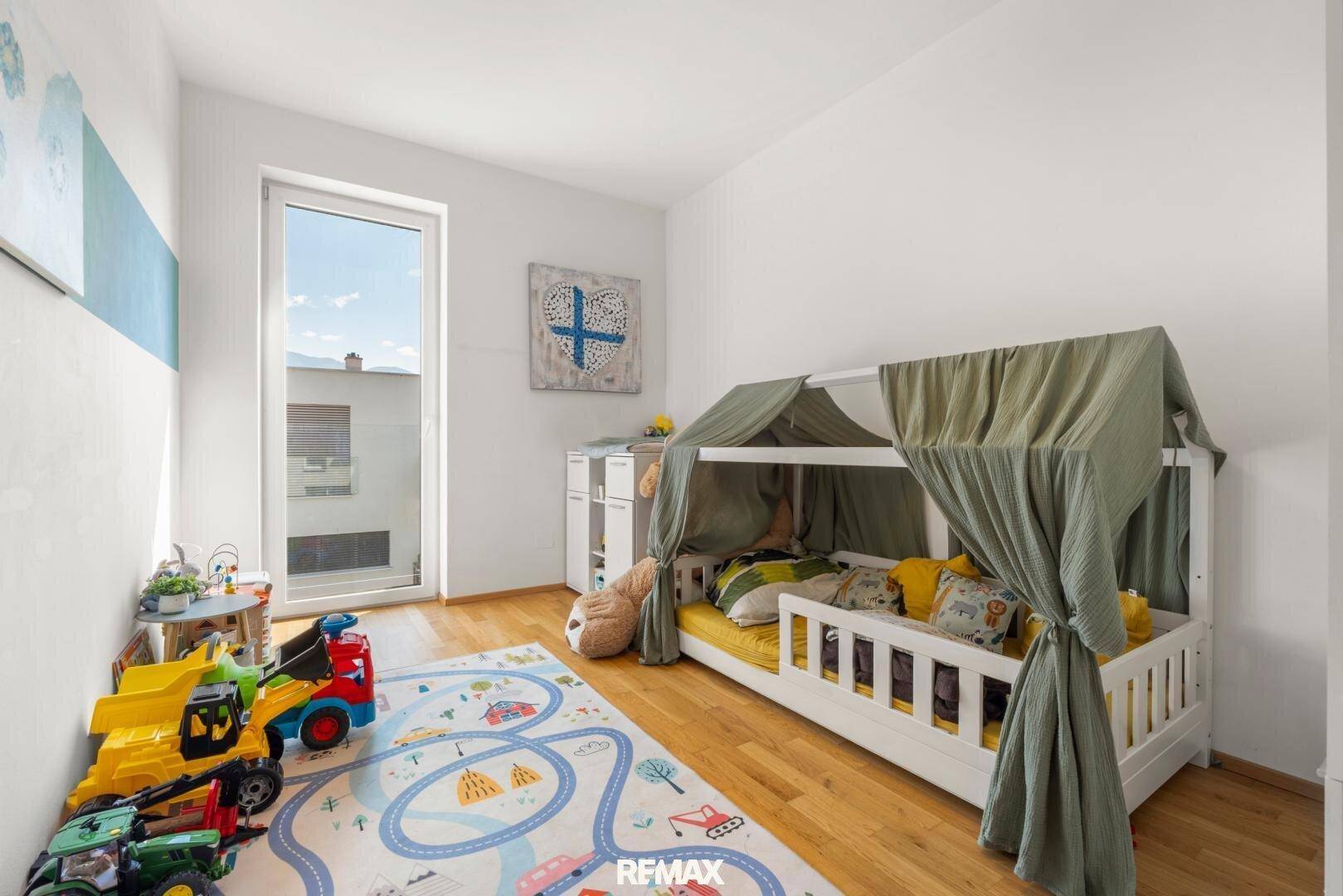 Freundliches Kinderzimmer mit Holzboden, Spielteppich und einem Bett mit Baldachin.