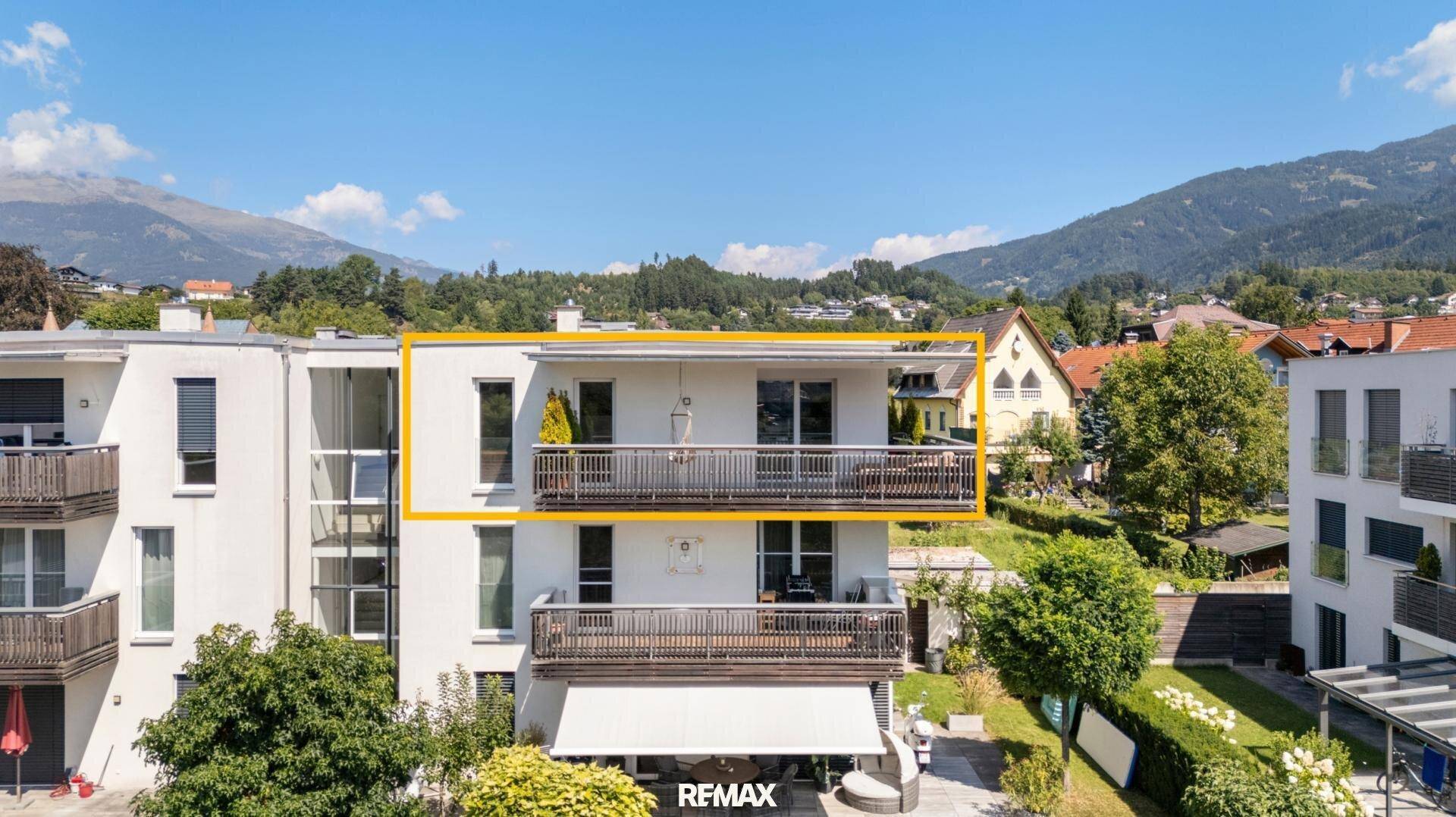 Moderne Gebäudefassade mit Balkonen und Blick auf die Berge im Hintergrund.