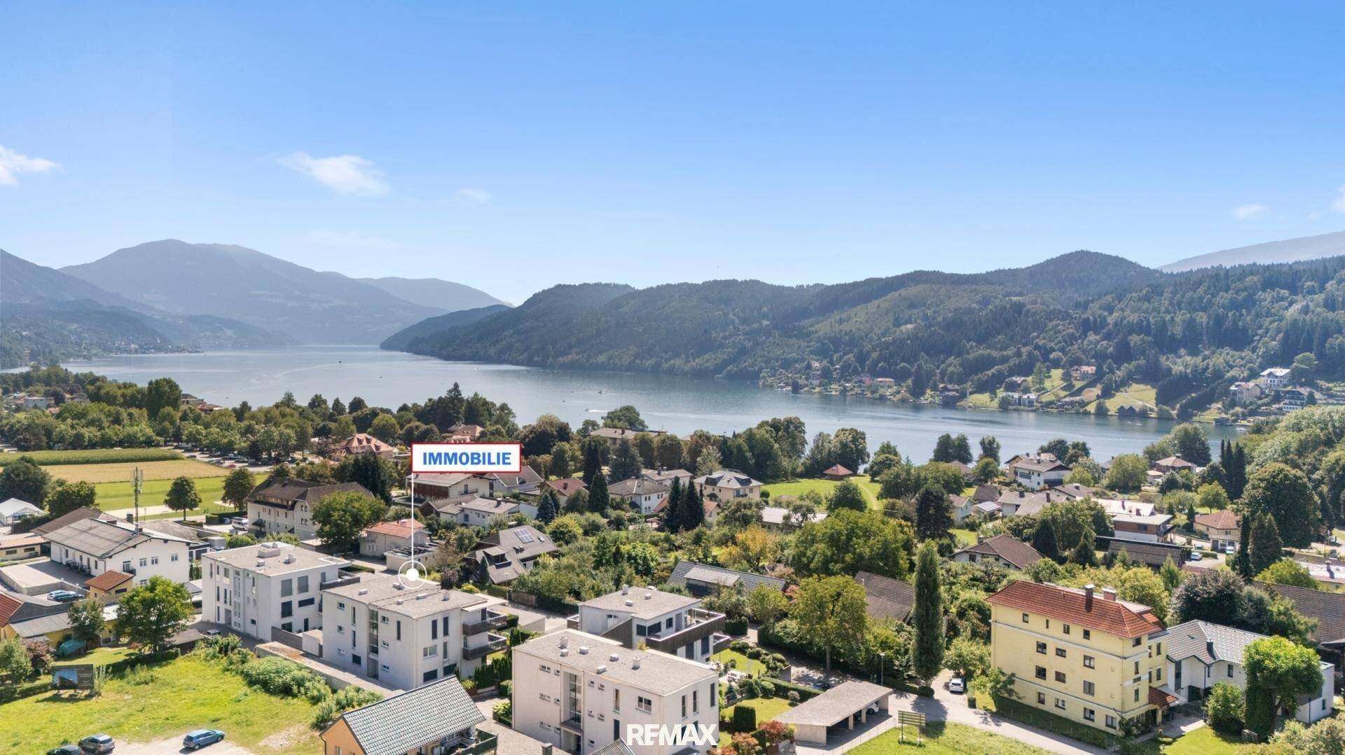 Weitläufige Luftaufnahme der Wohnanlage mit See- und Bergblick unter blauem Himmel.