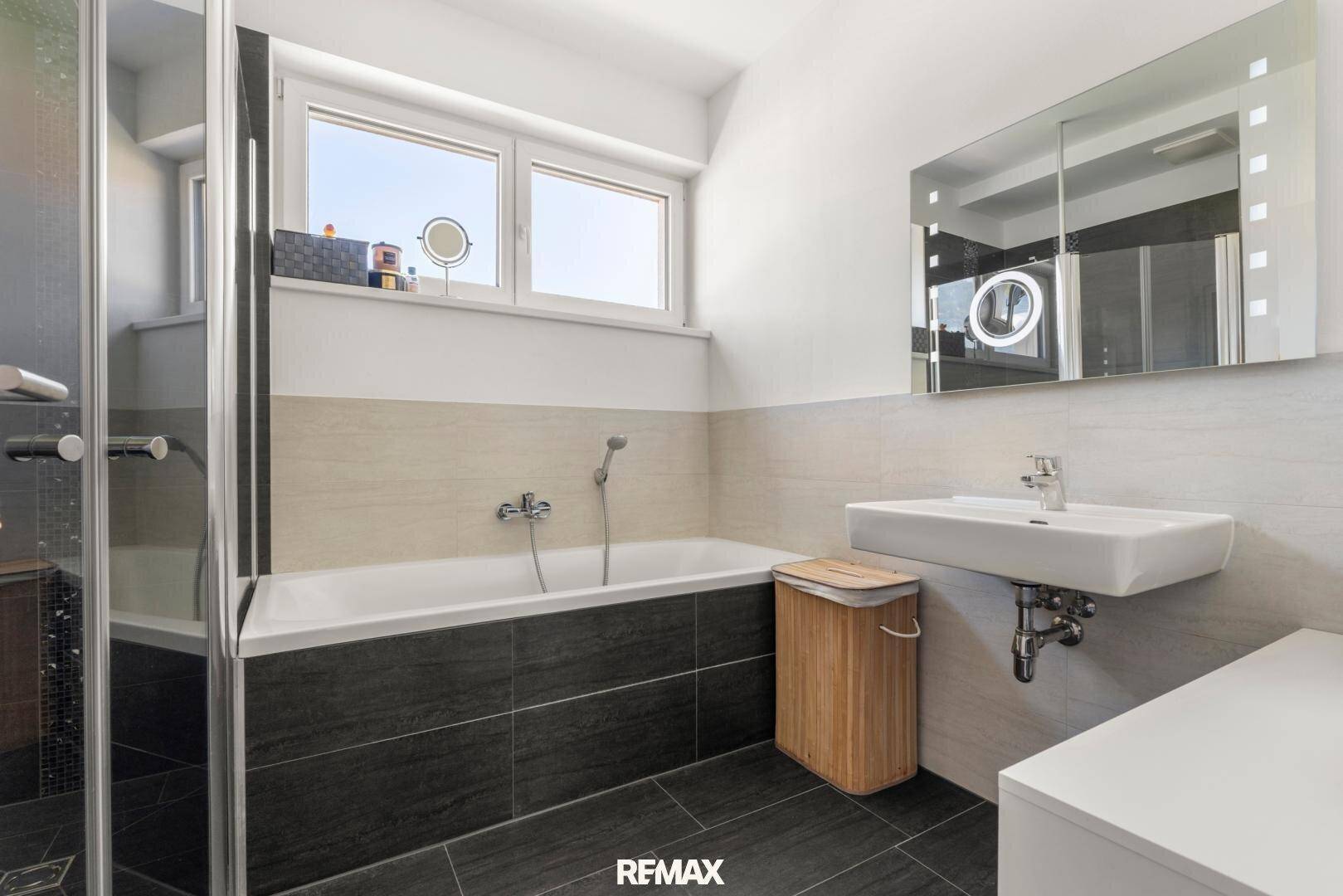 Modernes Badezimmer mit Badewanne, Duschkabine, Waschbecken und Fenster für Tageslicht.