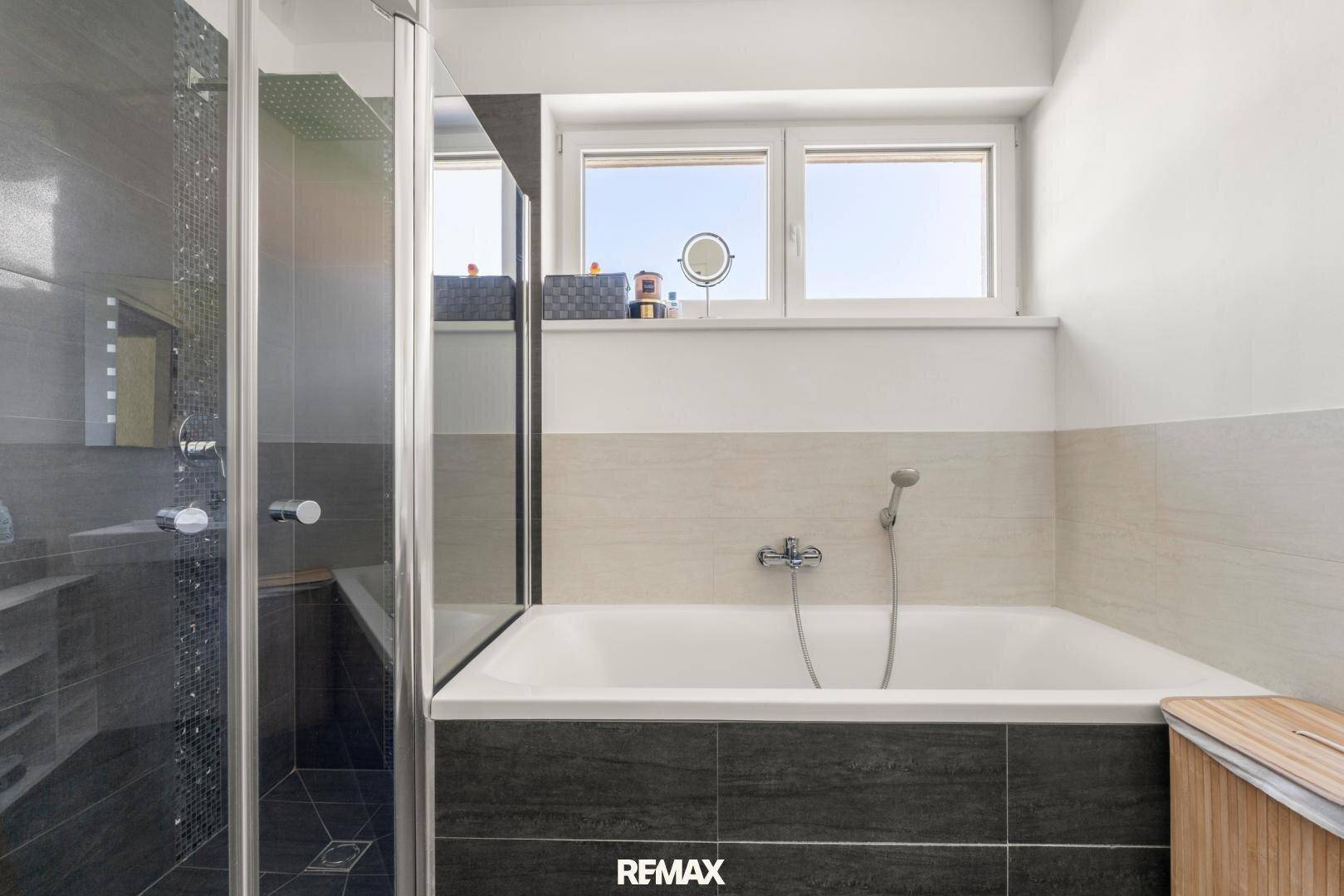Helles Badezimmer mit Badewanne, Duschkabine und Fenster, ausgestattet mit modernen Fliesen.