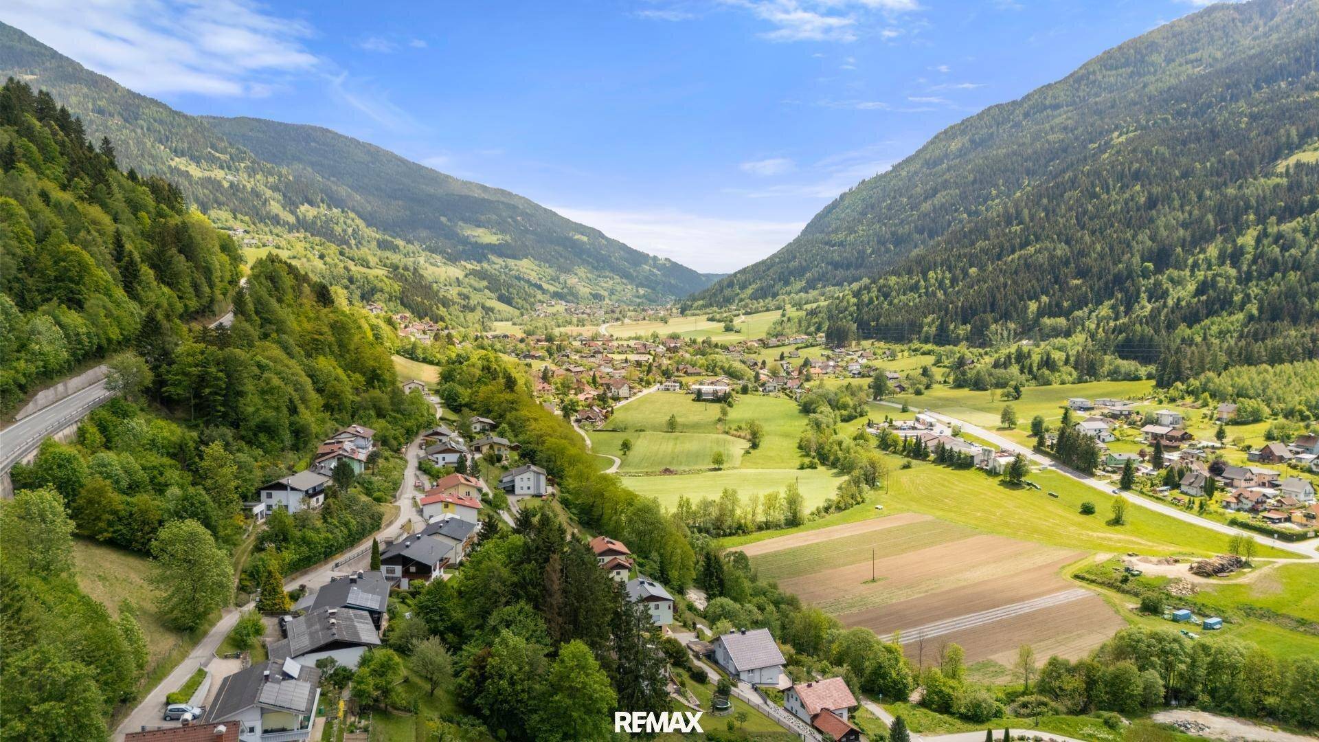 Weitläufige Luftaufnahme des Tals mit Siedlungen, Feldern und bewaldeten Bergen.