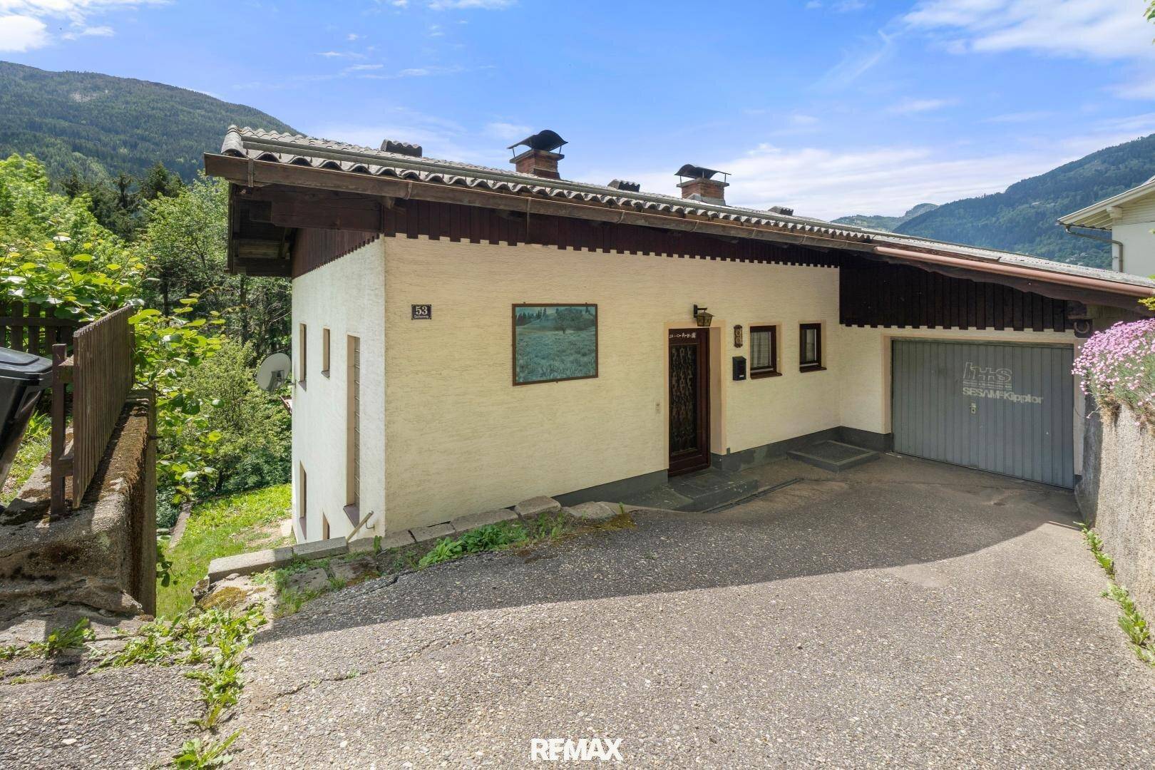 Seitenansicht des Hauses mit Eingangsbereich und Garage, eingebettet in die grüne Berglandschaft.
