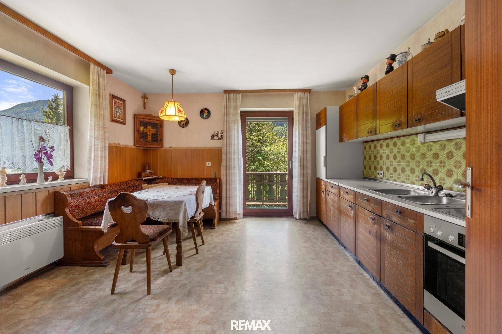 Traditionelle Wohnküche mit Holzeinbauten, Essbereich und Zugang zum Balkon mit Bergblick.