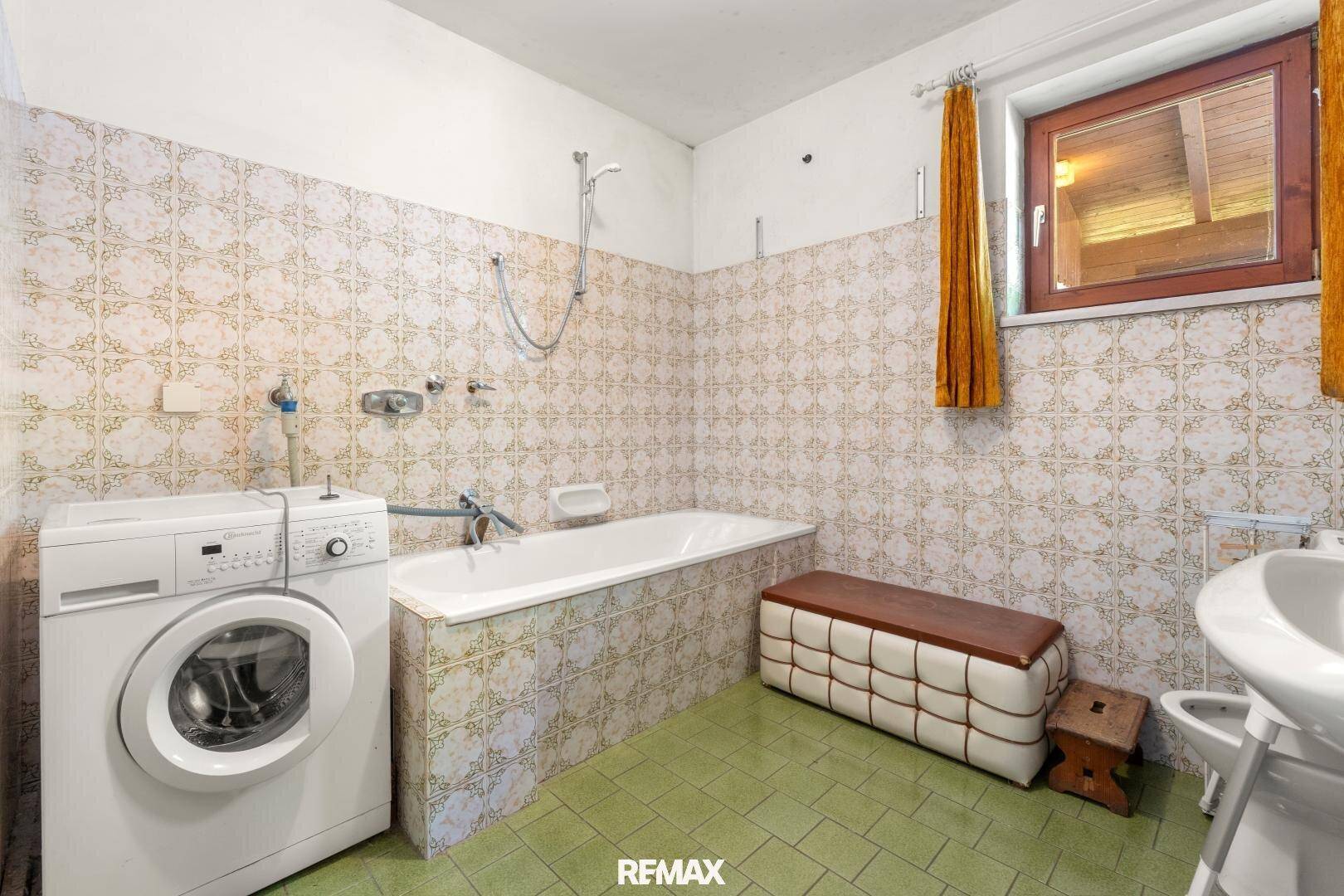 Badezimmer mit Badewanne, Waschmaschine, Bidet und Fenster, gefliest im 80er-Jahre-Stil.