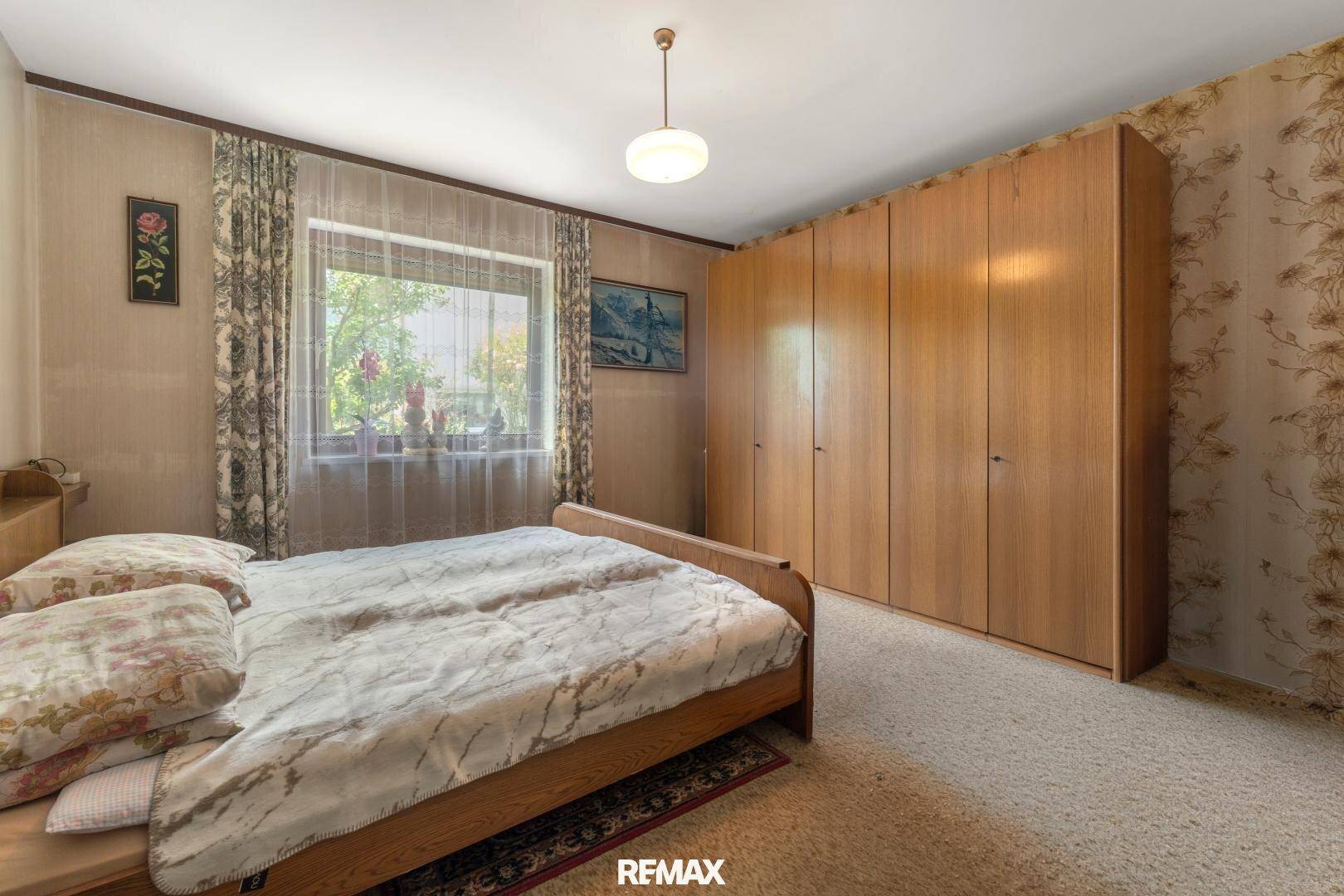 Helles Schlafzimmer mit Einbauschränken, Teppichboden und Fenster mit Blick auf die Natur.
