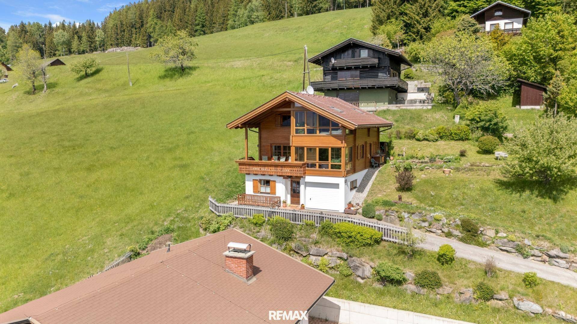 Charmantes Holzhaus am Hang mit mehreren Etagen, großen Fenstern und einem kleinen Balkon.