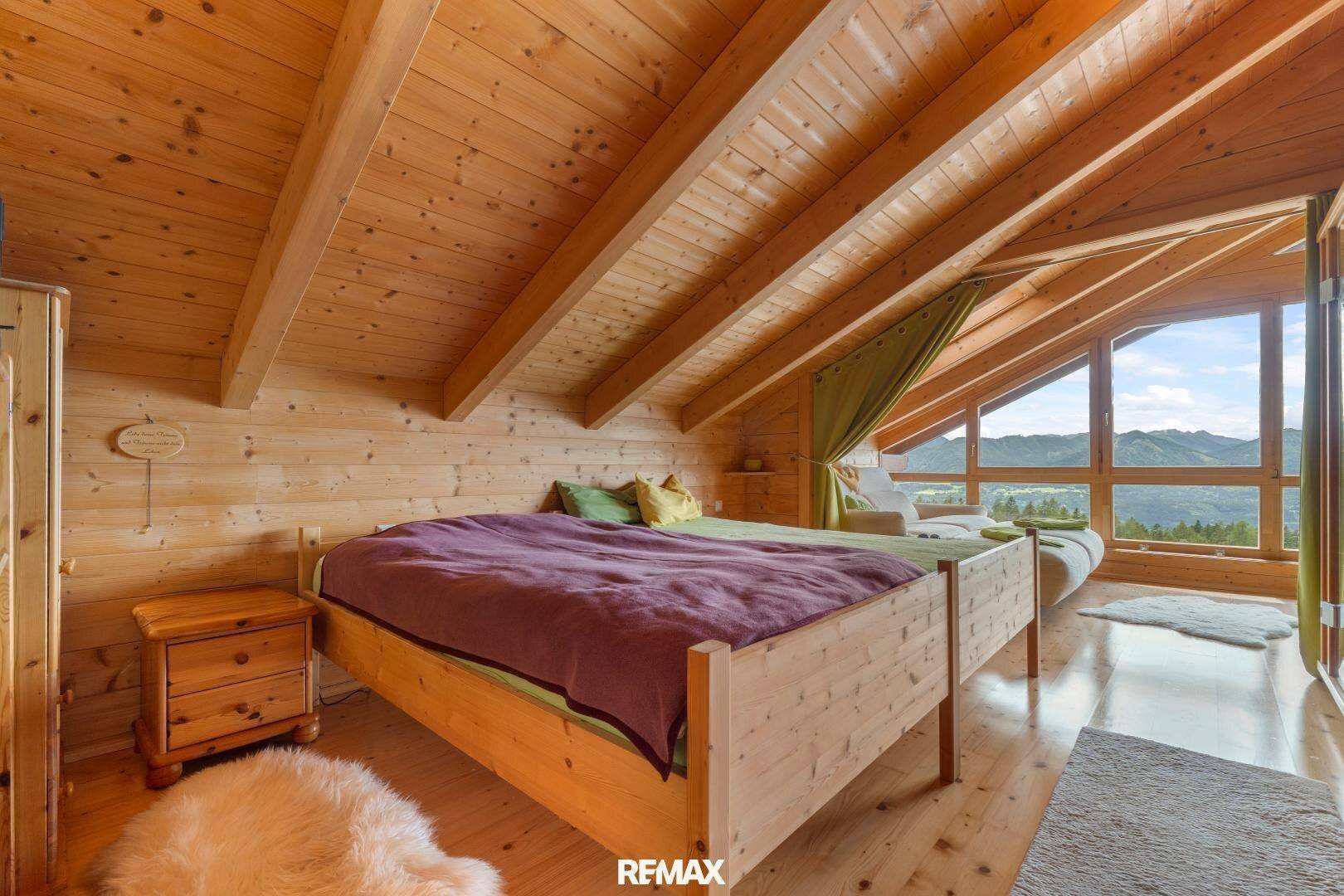 Gemütliches Schlafzimmer mit Holzwänden, Dachschräge und großem Fenster mit Bergblick.