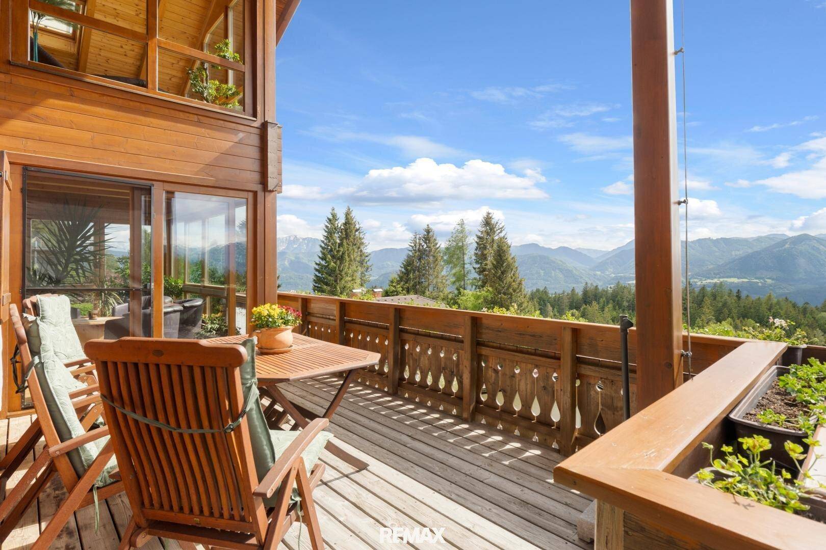 Großer Holzbalkon mit Sitzgelegenheiten und weitem Blick auf die alpine Landschaft.