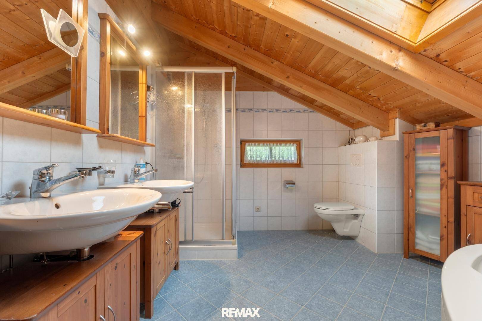 Helles Badezimmer mit Doppelwaschbecken, Dusche, Dachschräge und Holzmöbeln.