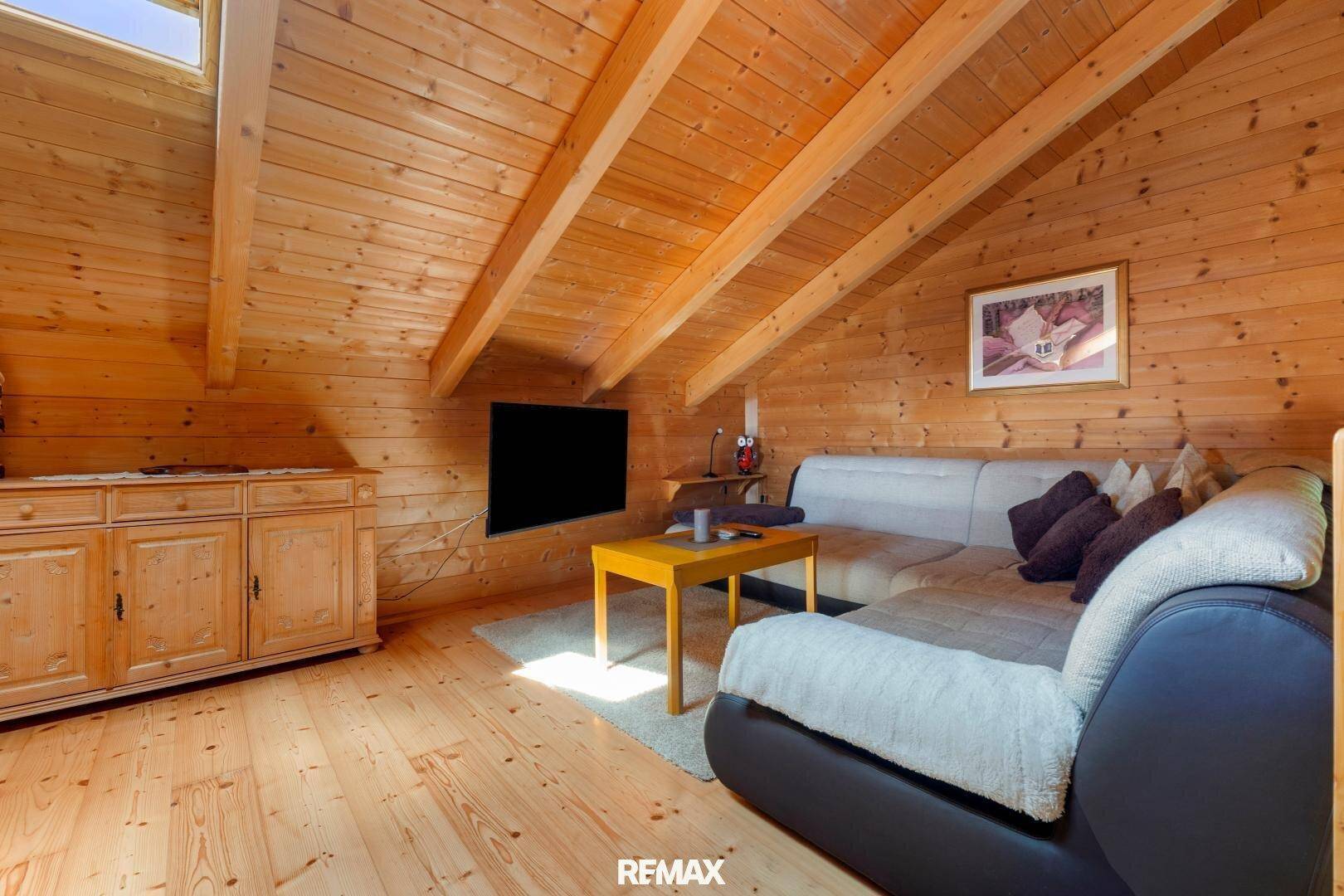 Gemütliches Wohnzimmer mit Holzwänden, Dachschräge und Sofa unter dem Dachfenster.