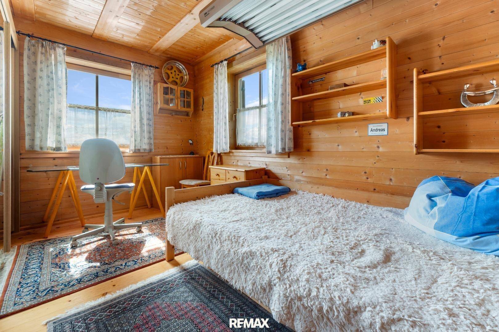 Kinderzimmer mit Holzwänden, Schreibtisch und zwei Fenstern mit Blick ins Grüne.