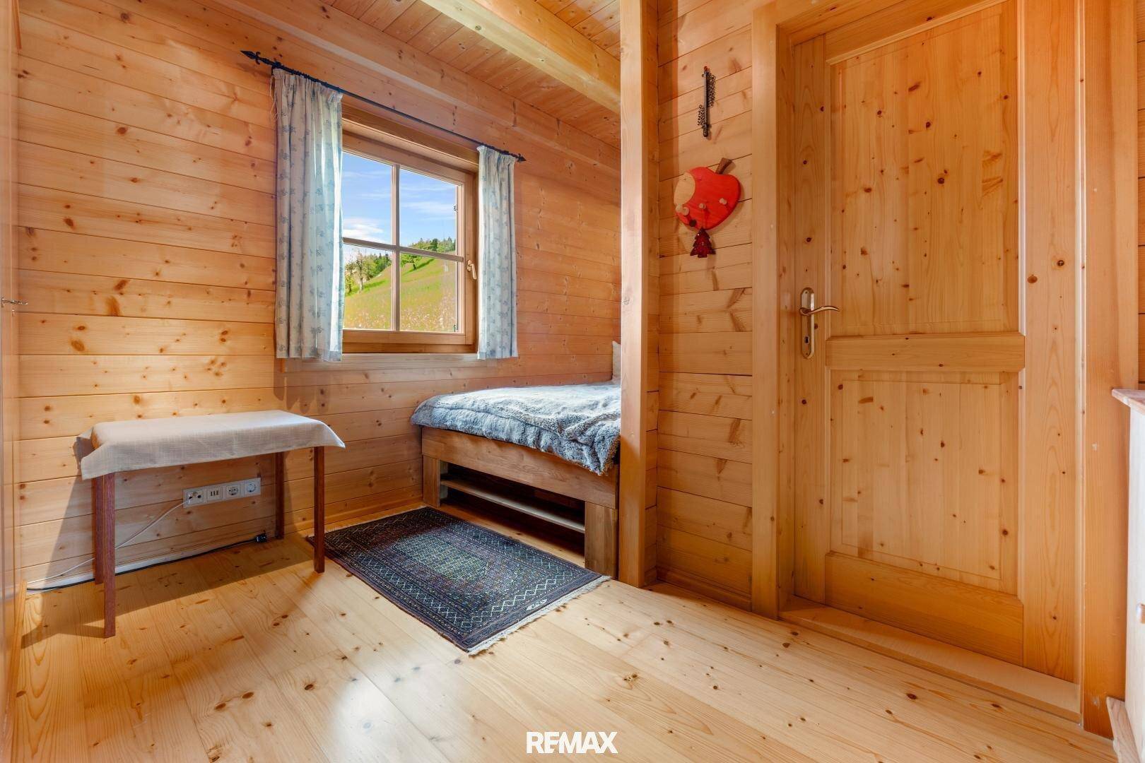 Kleines Schlafzimmer oder Alkoven mit Holzwänden und Fenster mit Blick ins Grüne.