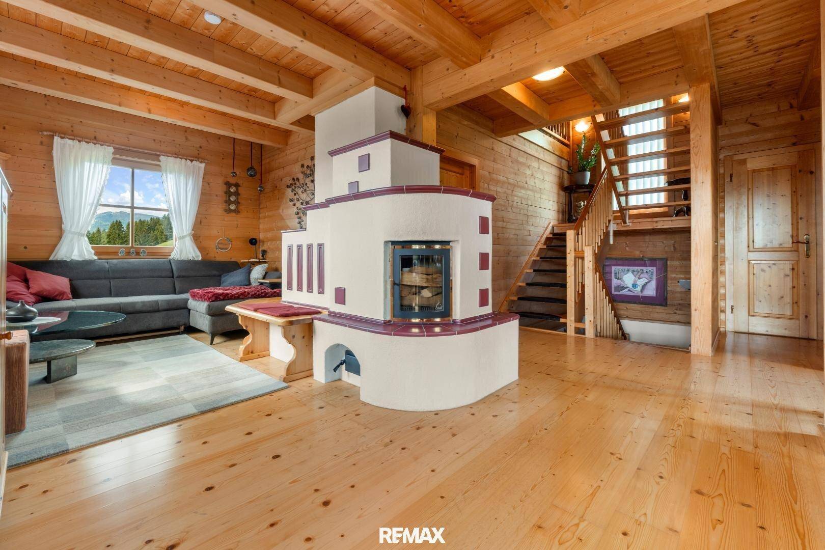 Geräumiger Wohnbereich mit Kachelofen, Holzvertäfelung und offener Treppe.