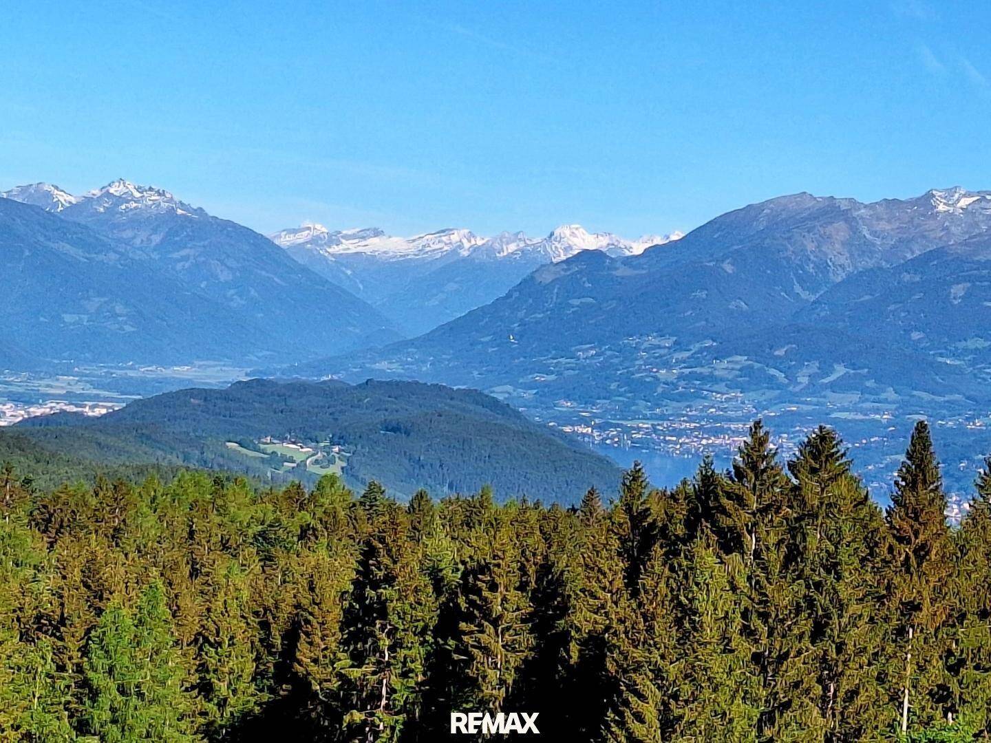 Atemberaubender Ausblick auf schneebedeckte Berge, ein Tal mit See und dichte Wälder im Vordergrund.