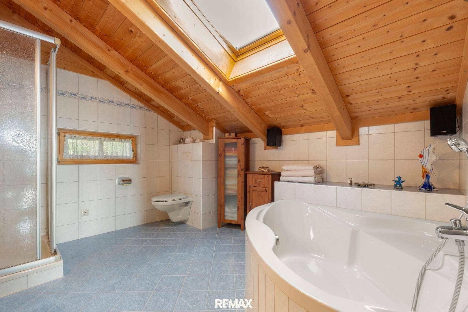 Geräumiges Badezimmer mit Badewanne, Dusche, Dachfenster und Holzbalken.