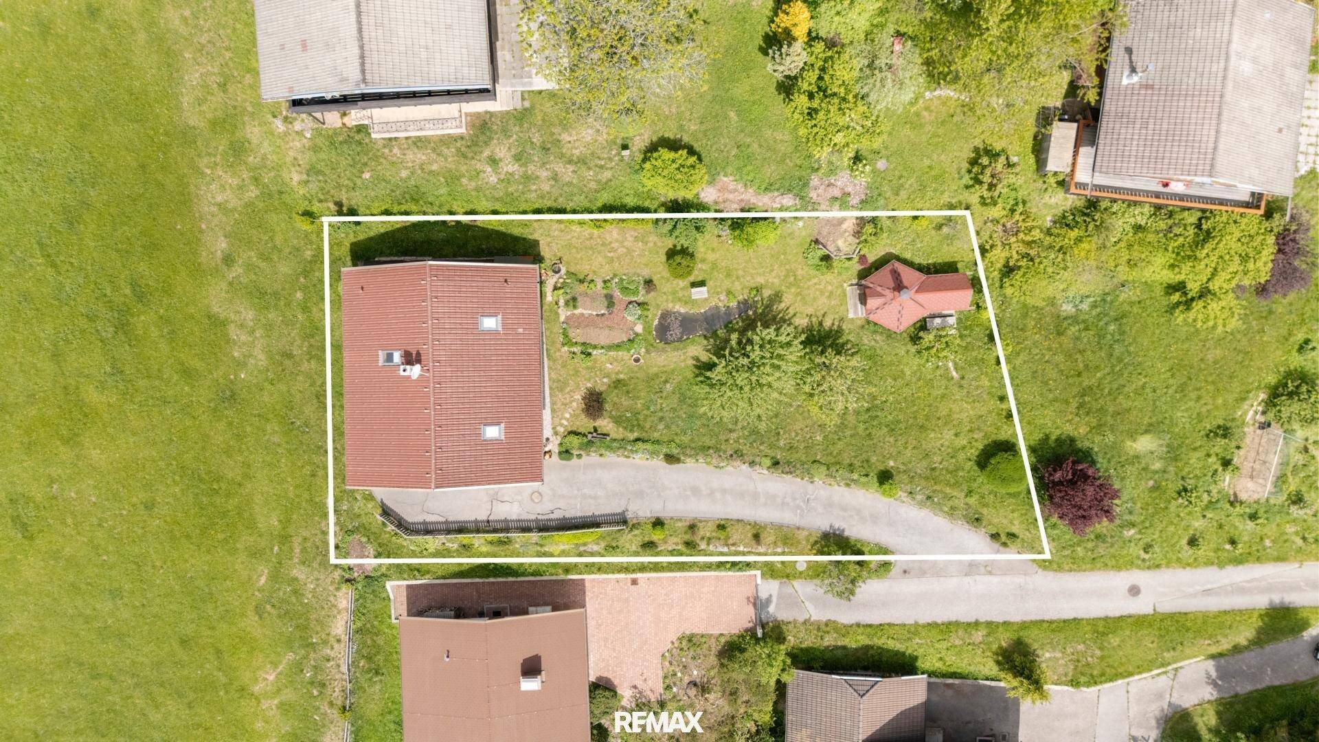 Vogelperspektive eines Grundstücks mit Haus, Gartenbereich und geschwungener Zufahrt, weiß umrandet.