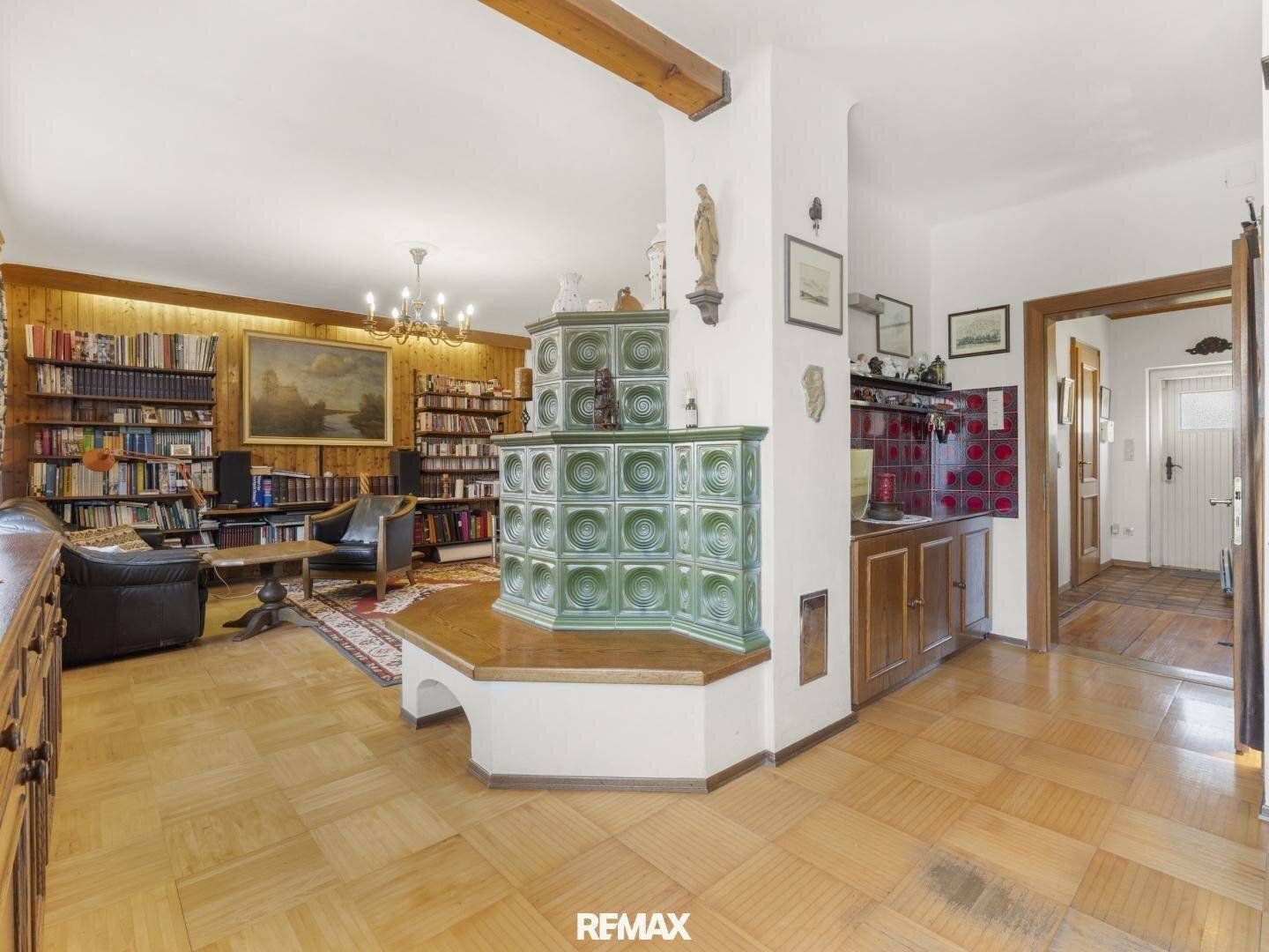 Gemütliches Wohnzimmer mit traditionellem Kachelofen, Holzbalken und umfangreicher Bibliothek.