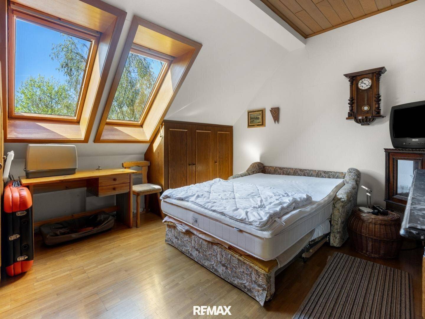 Helles Schlafzimmer im Dachgeschoss mit zwei großen Dachfenstern und Holzboden.