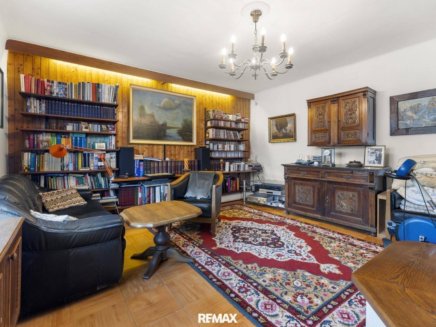 Traditionell eingerichtetes Wohnzimmer mit Holzwänden, Teppich und vielen Büchern in Regalen.