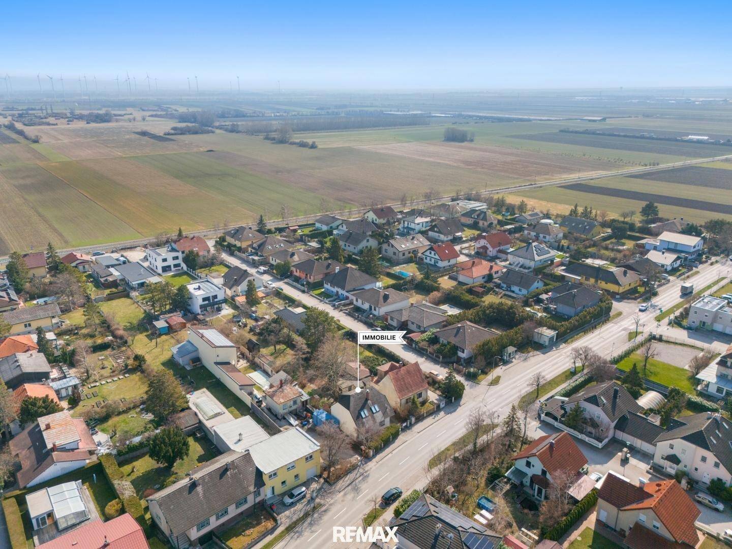 Luftaufnahme der Wohnsiedlung mit Feldern im Hintergrund und Windrädern am Horizont.