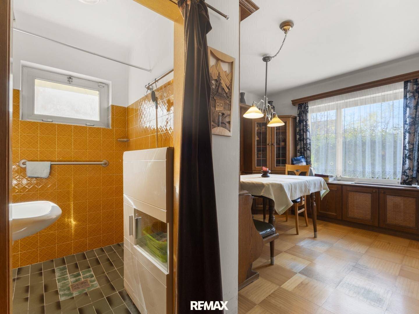 Badezimmer mit gelben Fliesen, Duschbereich und Waschbecken, angrenzend an den Essbereich.