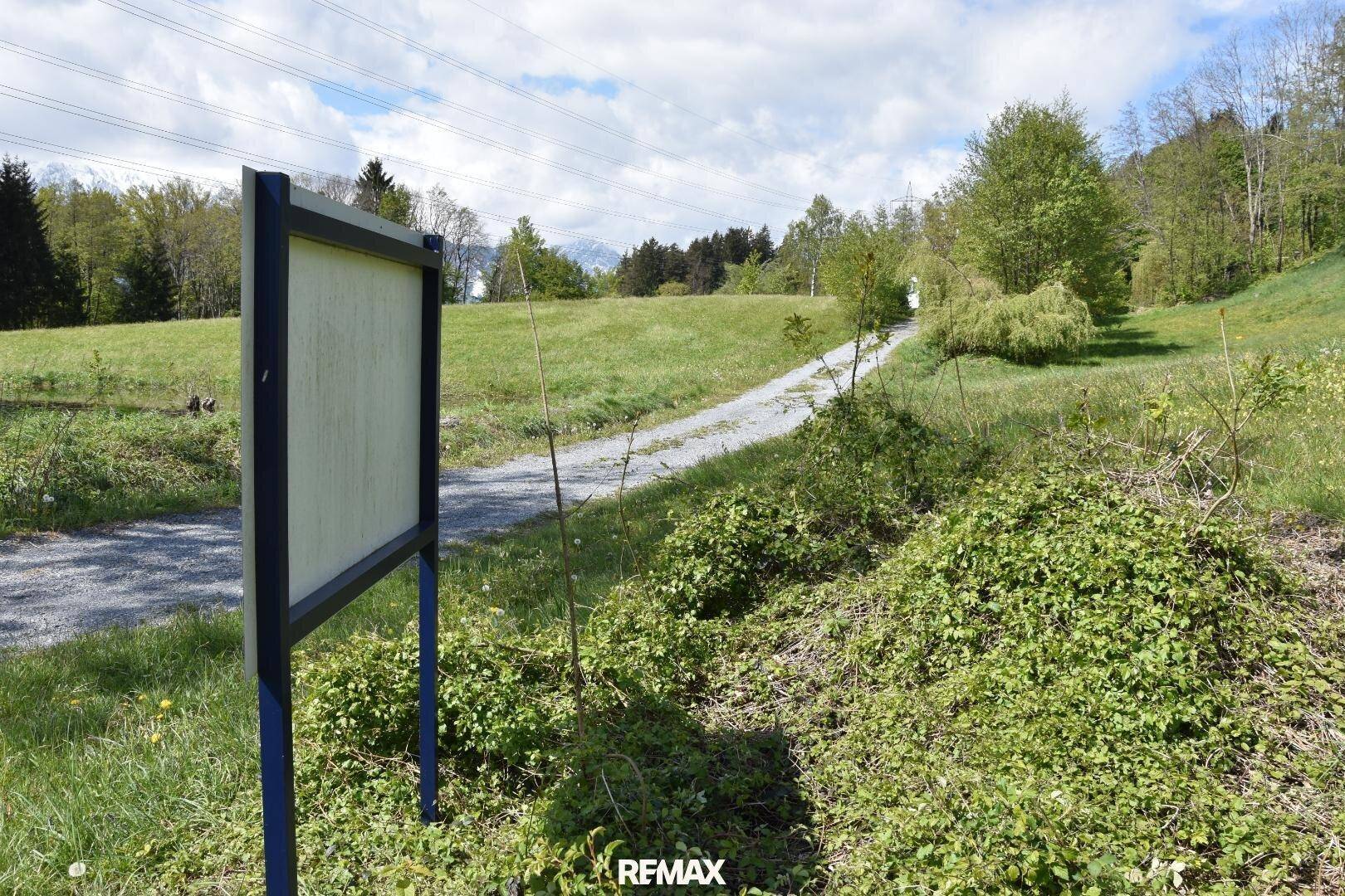Ein Schotterweg führt durch eine grüne Landschaft mit einem Informationsschild am Wegesrand.