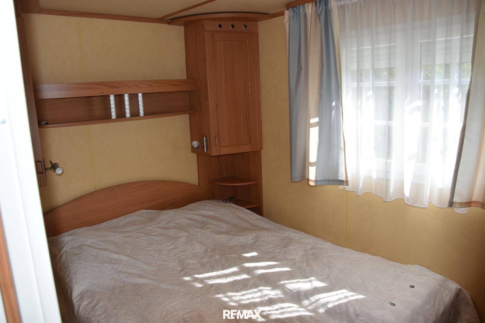 Helles Schlafzimmer mit Doppelbett, Holzmöbeln und einem Fenster mit Vorhängen.