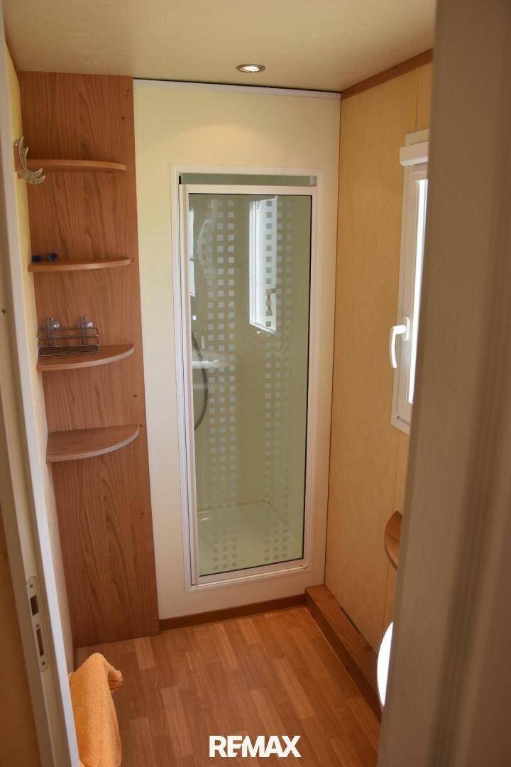 Kleines Badezimmer mit Duschkabine, Holzregalen und einem Fenster für Tageslicht.