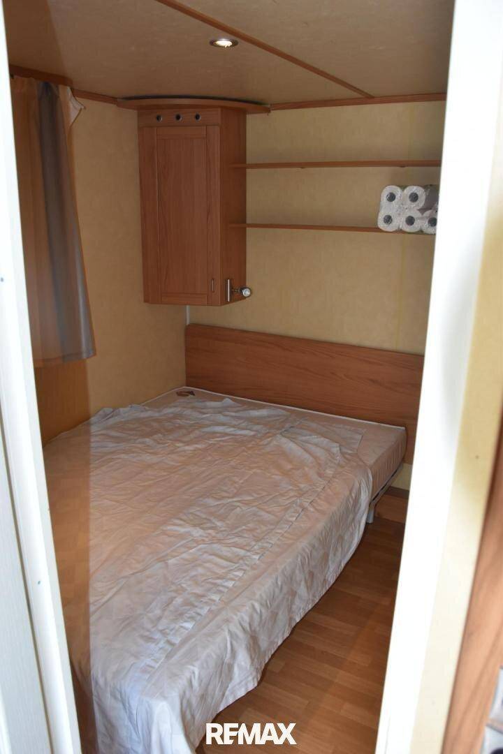 Schlafzimmer in einem Mobilheim mit Doppelbett, Holzvertäfelung und integrierten Schränken.