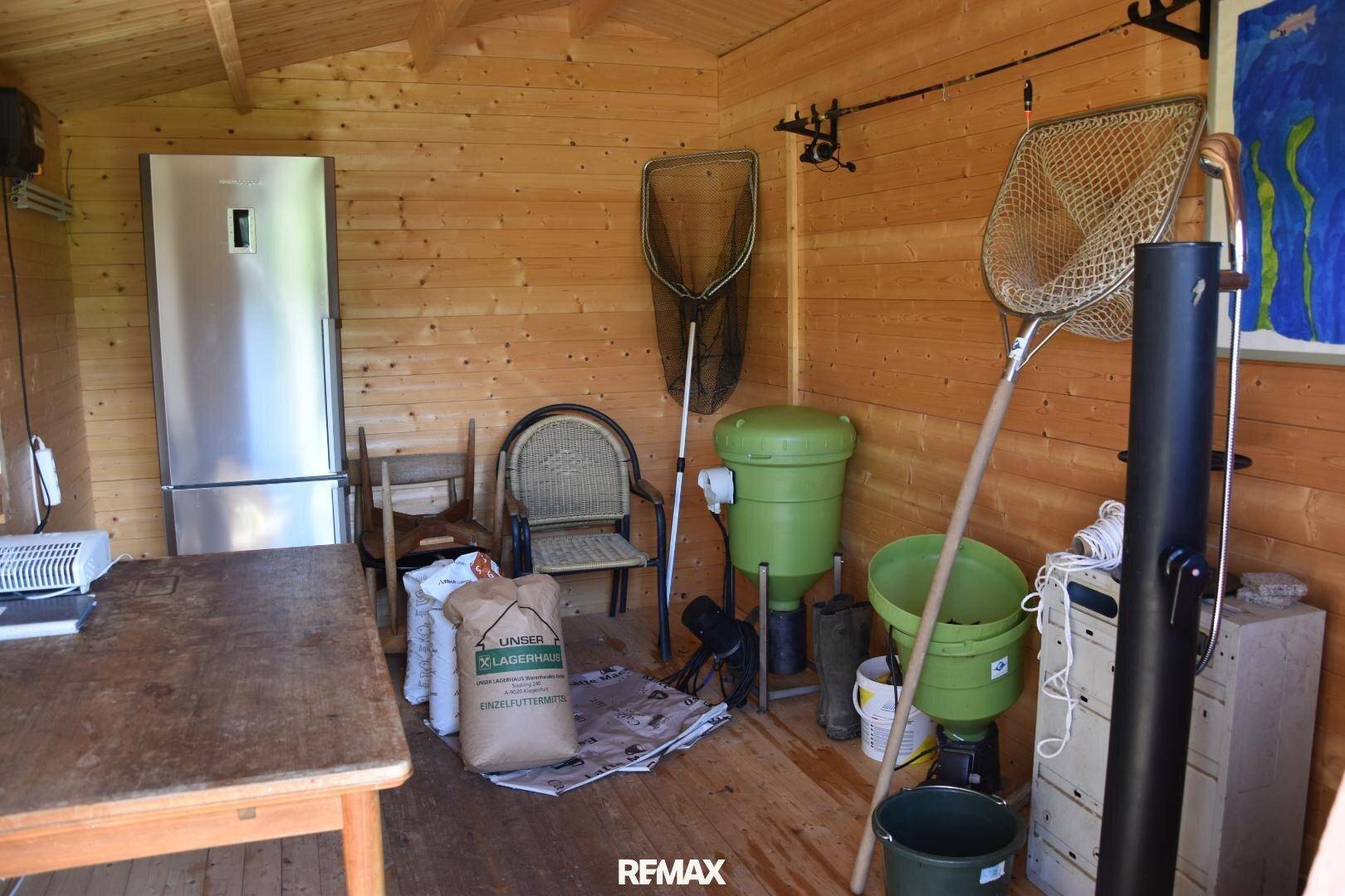 Innenansicht einer Holzhütte mit Kühlschrank, Angelzubehör und verschiedenen Geräten.