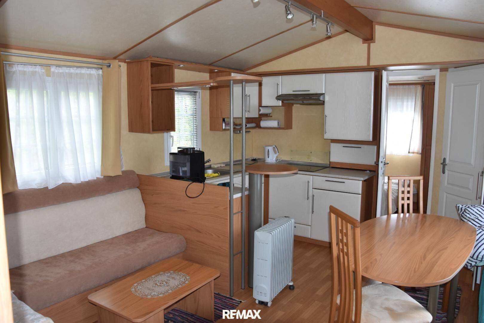 Heller Wohnbereich mit Küchenzeile, Esstisch und Sofa, durch Fenster gut belichtet.