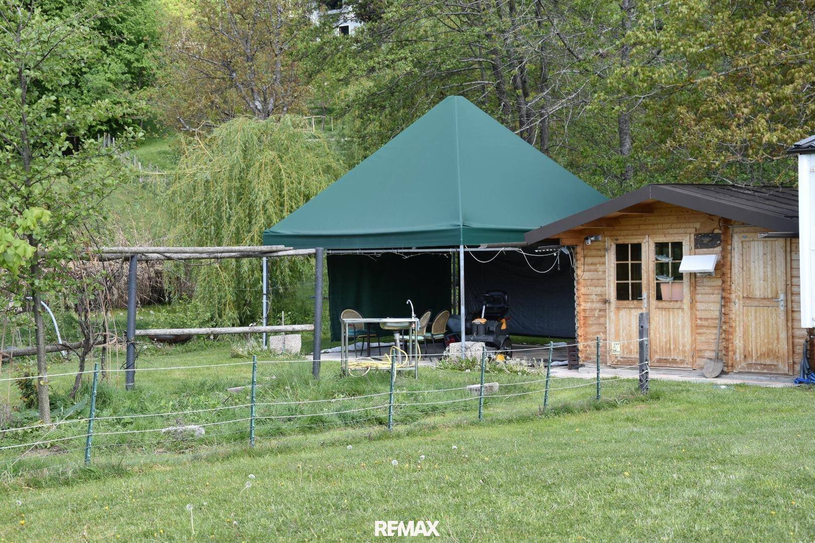 Gartenbereich mit einem grünen Partyzelt, einer Holzhütte und Sitzgelegenheiten im Freien.