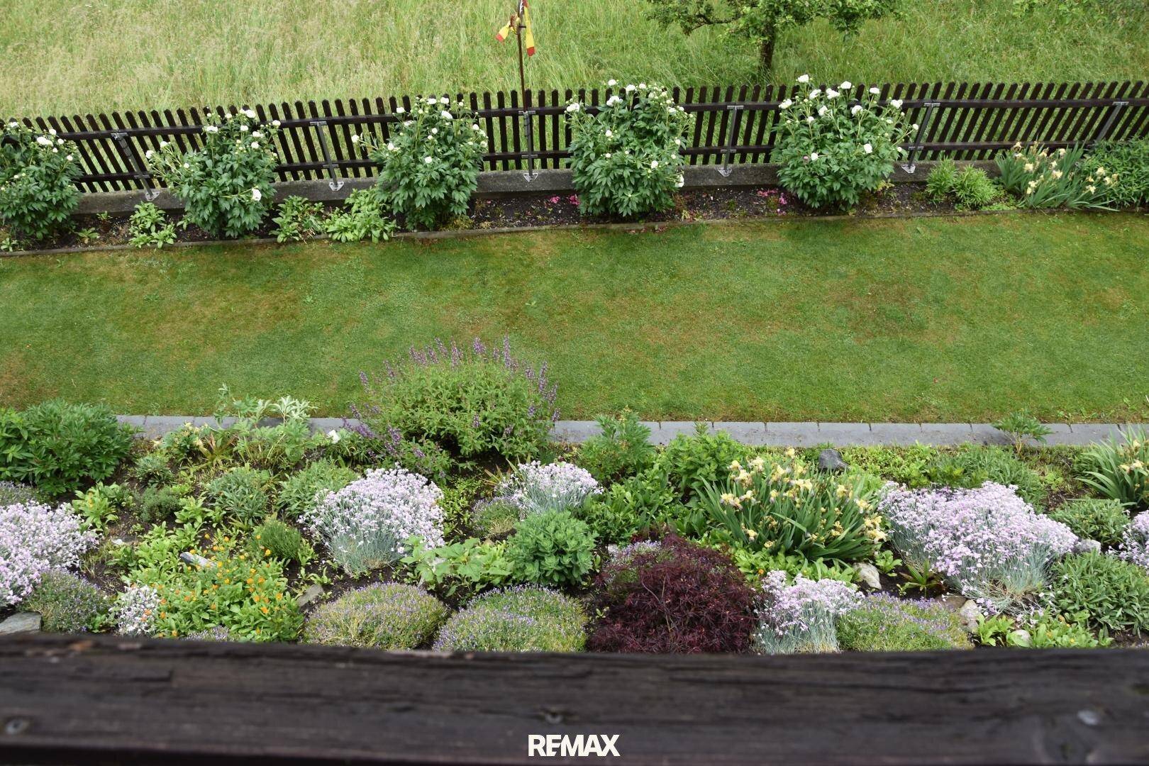 Gepflegter Garten mit bunten Blumenbeeten und Rasenfläche, von oben betrachtet.