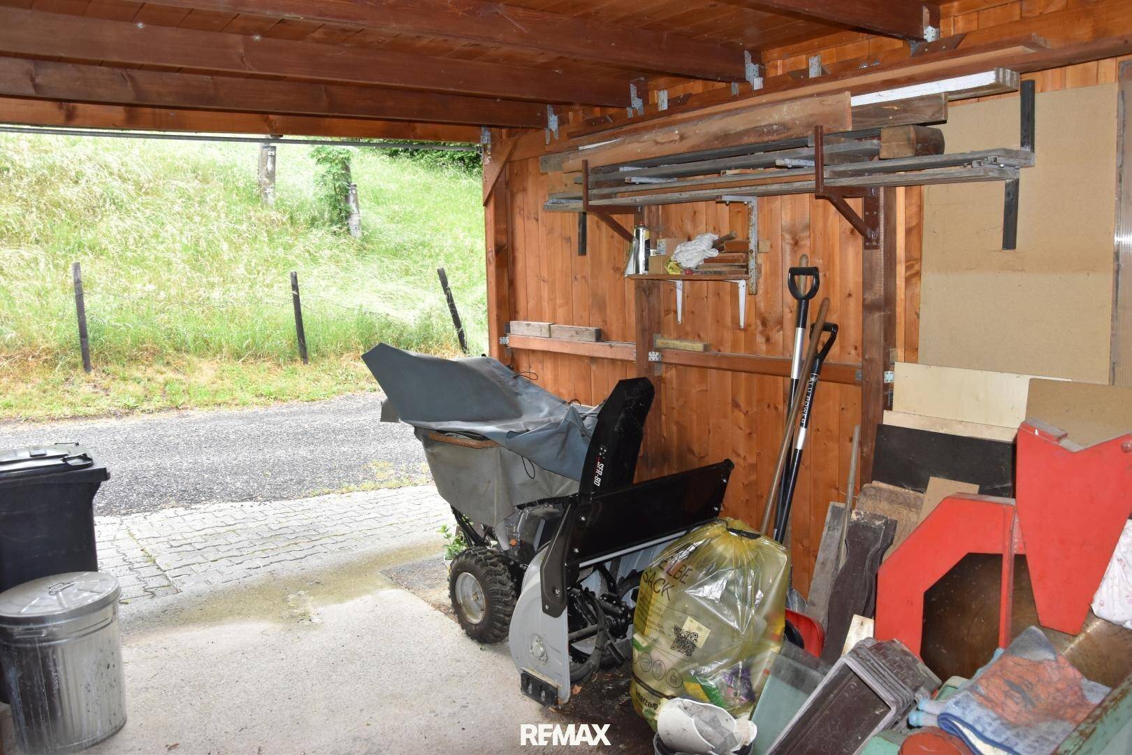 Überdachter Außenbereich aus Holz, genutzt als Abstellfläche für Geräte und Materialien.