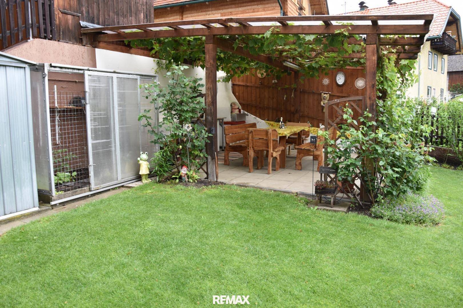 Gepflegter Garten mit Rasenfläche und überdachtem Sitzbereich unter einer bewachsenen Holzpergola.