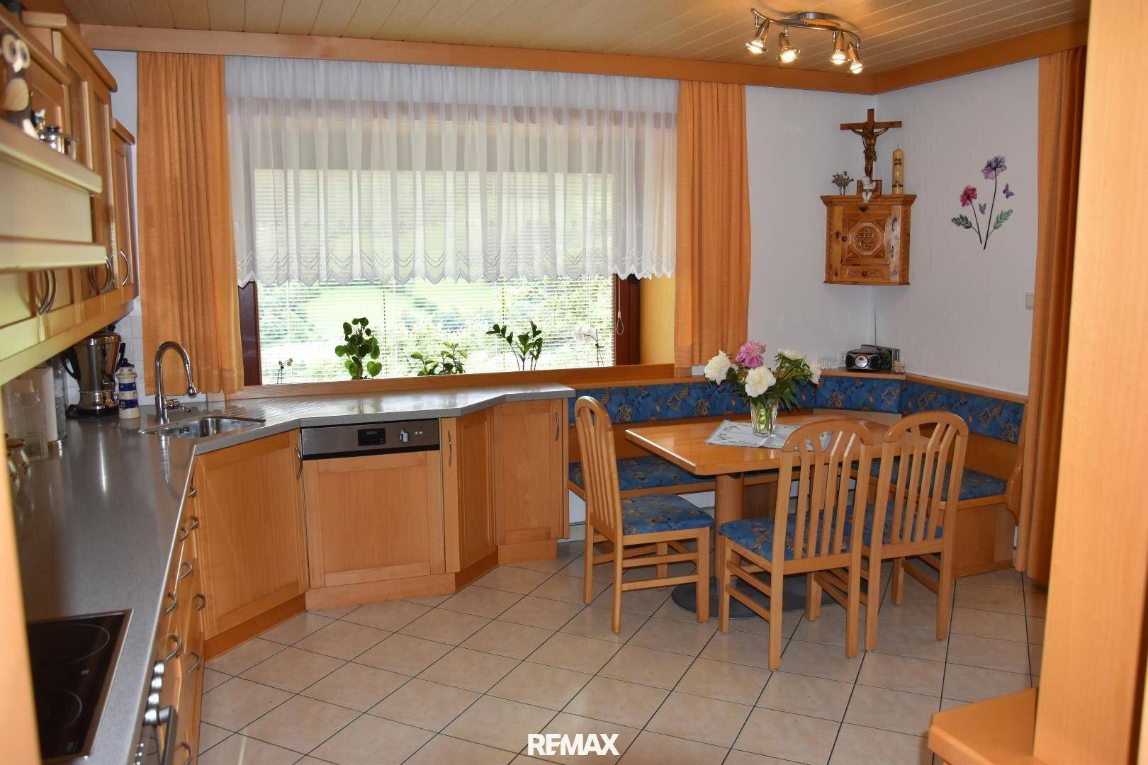 Helle Küche mit Holzeinbauten, integrierter Essecke und Blick ins Grüne durch das Fenster.