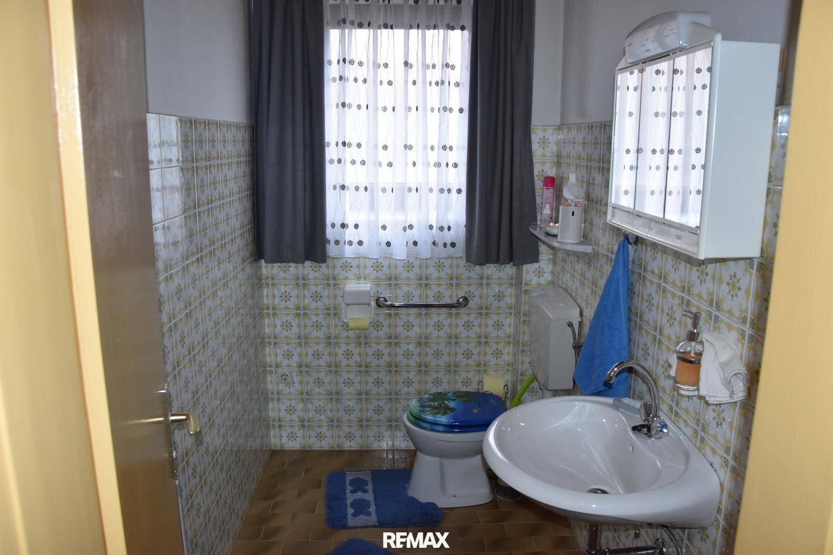 Badezimmer mit gemusterten Fliesen, WC, Waschbecken und Haltegriffen für mehr Sicherheit.