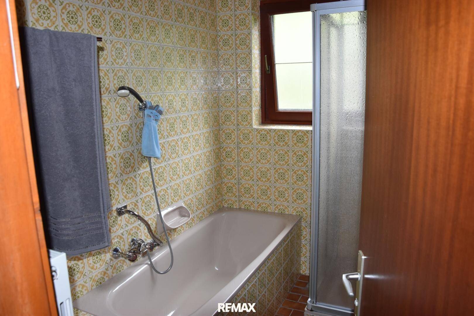 Badezimmer mit Badewanne, Duschabtrennung und gemusterten Fliesen, funktional eingerichtet.
