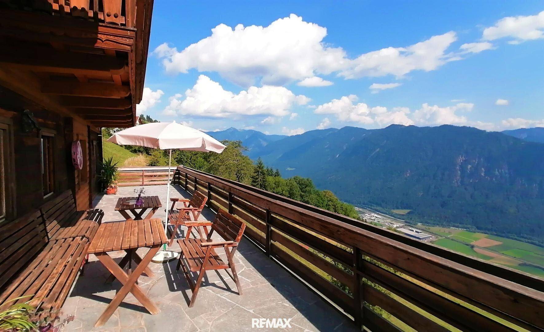 Gemütliche Terrasse mit Holztisch, Stühlen und Sonnenschirm, die einen spektakulären Blick auf die Berge und das Tal bietet.