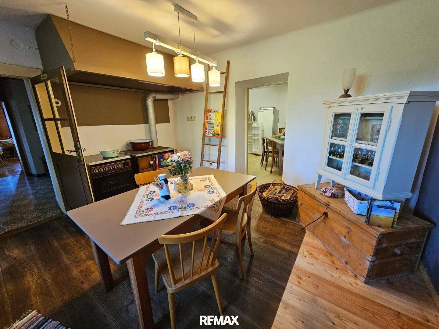 Rustikale Wohnküche mit traditionellem Holzofen, Holztisch und Stühlen, sowie einem Schrank und einer Leiter.