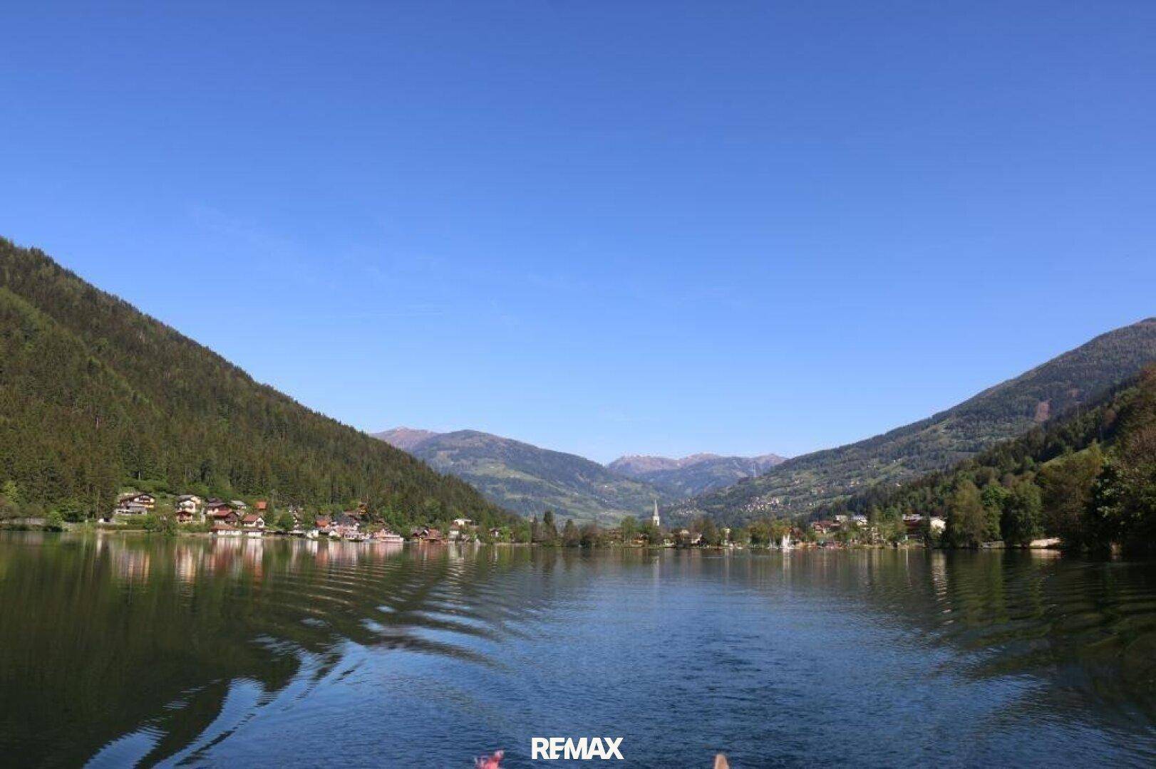Weitläufiger, ruhiger Blick über den See, der den Himmel und die Berge widerspiegelt.