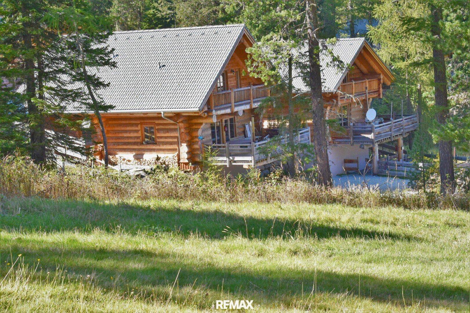 Rustikales Holzchalet inmitten einer grünen Wiese und umgeben von hohen Bäumen.