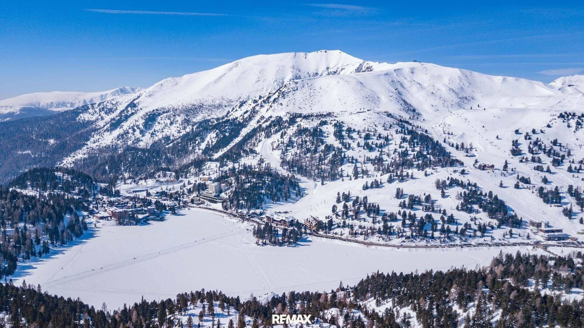 Beeindruckende Luftaufnahme einer verschneiten Bergregion mit zugefrorenem See und Siedlung.