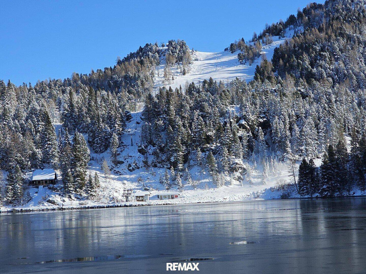 Winterliche Berglandschaft mit gefrorenem See und schneebedeckten Wäldern am Ufer.