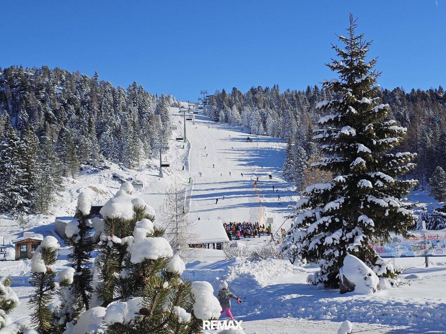 Belebtes Skigebiet mit Piste, Lift und vielen Skifahrern in der winterlichen Bergwelt.
