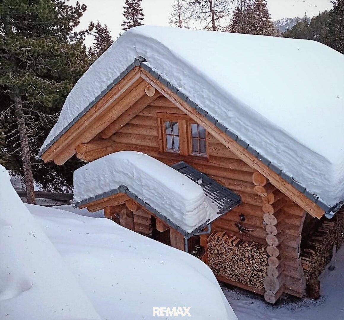 Rustikales Holzchalet mit schneebedecktem Dach und einem großen Holzstapel an der Seite.